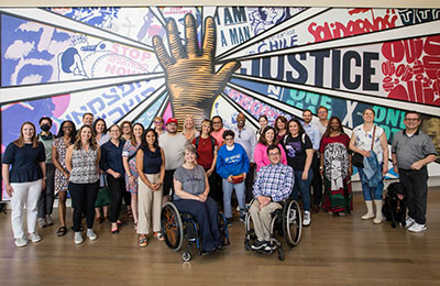 A group of people standing/sitting in front of an art mural of civil rights leaders.